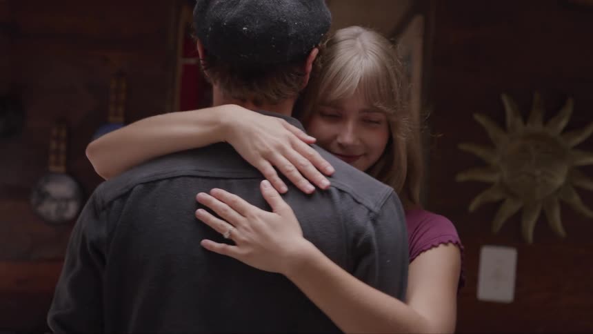 The video shows a man and a woman embracing in a close loving hug the woman with long blonde hair puts her arms around the mans neck and rests her head on his shoulder