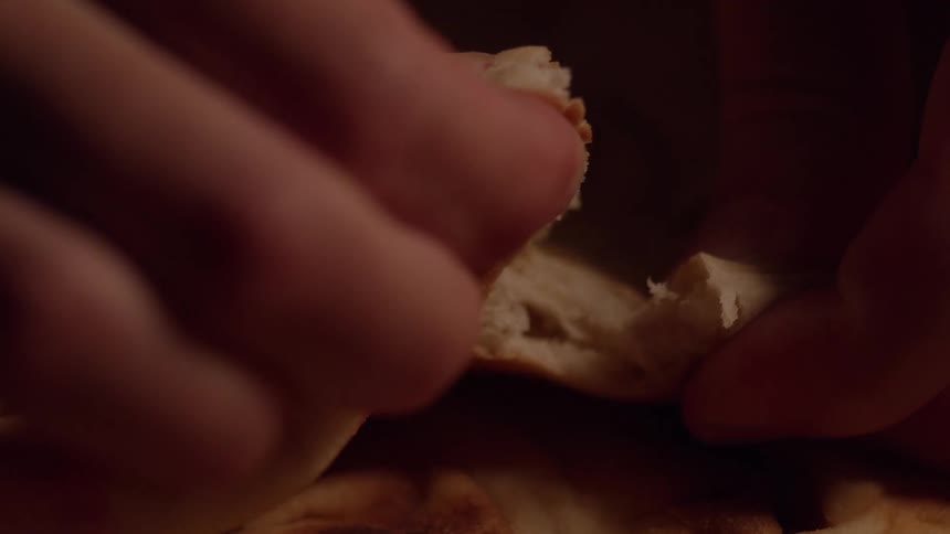 Hands gently tear fresh bread in a warm intimate closeup