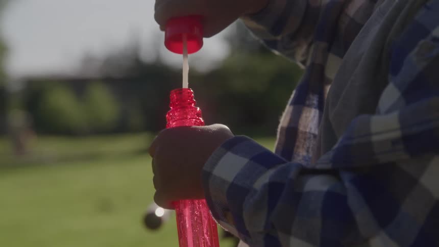 Childs hands dip and pull a wand from a bright red bottle readying more bubbles in a sunny field
