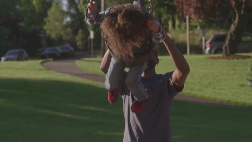 Father pushes his young son on a swing in the park