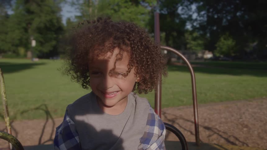 Child smiles while sitting on playground equipment outdoors