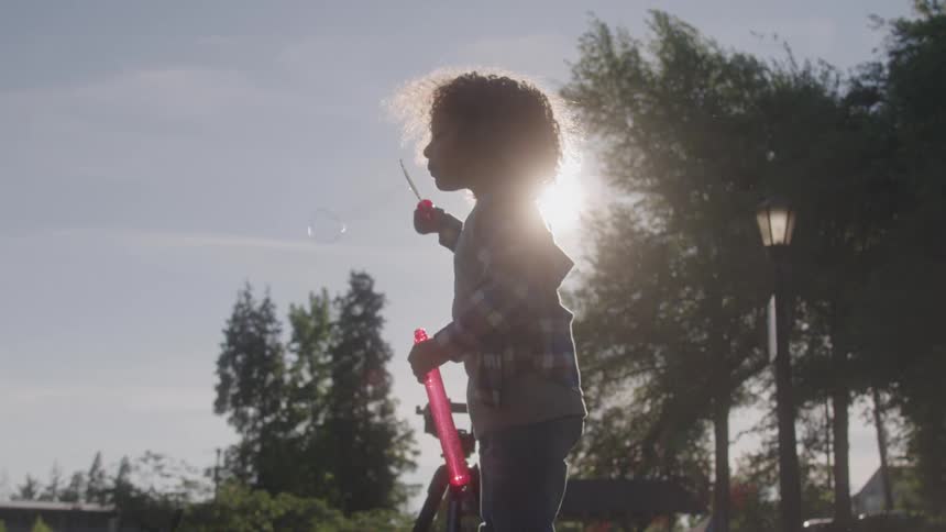 A child is blowing bubbles outside while standing in the sunlight
