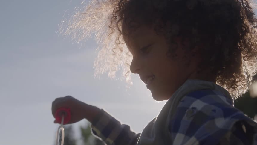 Child blows soap bubbles outdoors under sunlight