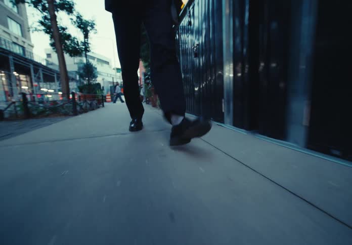 A person walks along a sidewalk past a building and some potted plants