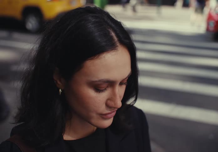 A woman stands on a busy city street looking thoughtful