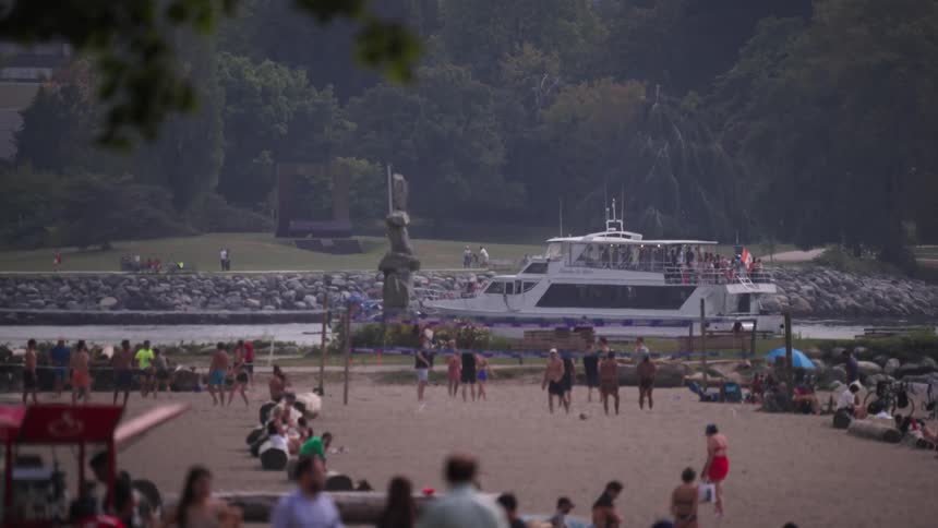 The video shows a wide shot of a crowded beach on a cloudy day in the background a large white boat is sailing past in the harbor