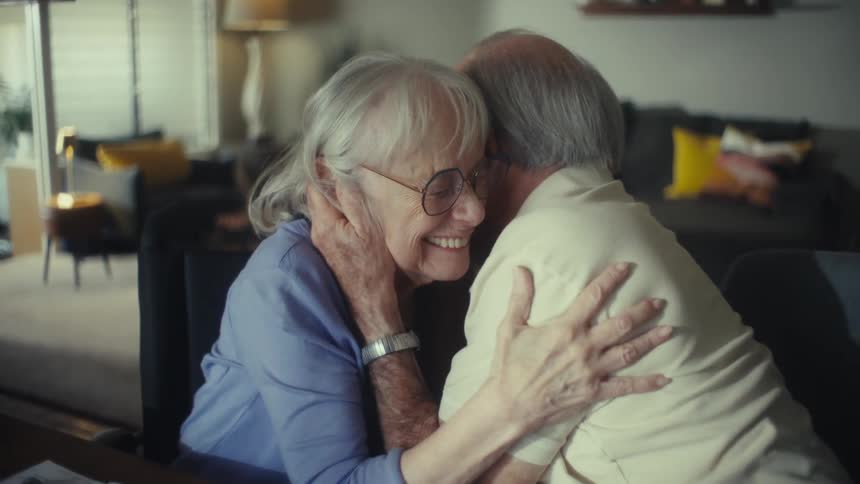 Elderly couple hugs with emotion and smiles at home