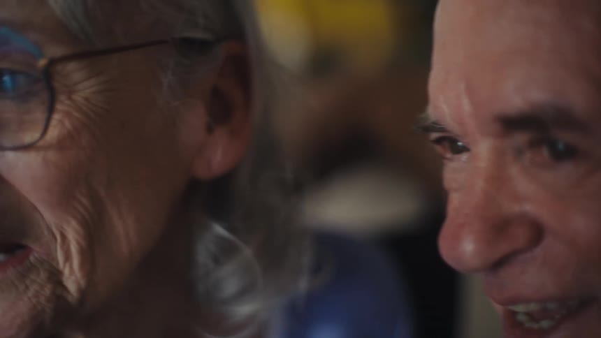 An elderly couple sits closely together having a fun discussion that makes them smile with the woman wearing glasses at midday
