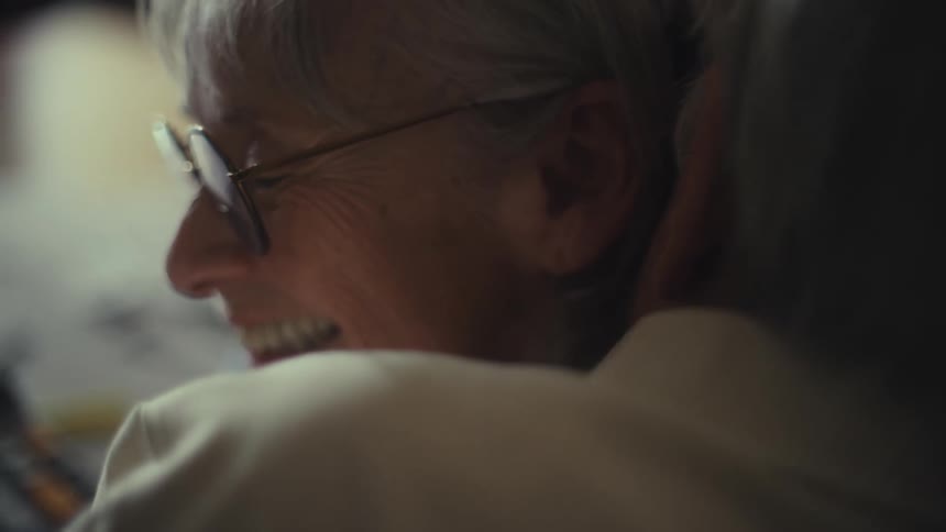 The video shows a closeup shot of a persons face possibly a woman with short white hair she is smiling and wearing glasses