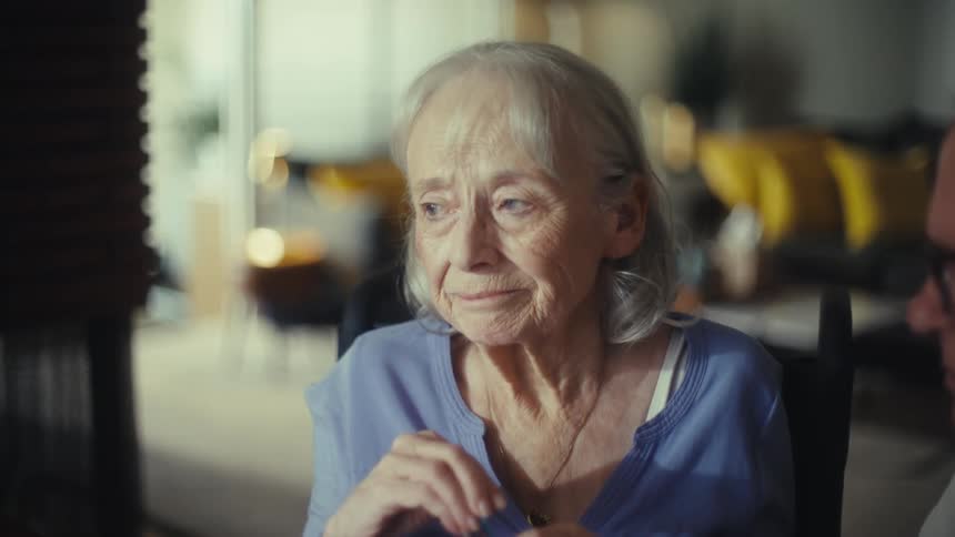 A woman with grey hair and glasses looks at paperwork takes her glasses off and then looks up with a worried expression