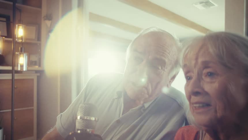 Elderly couple sits in front of a microphone at home during the day and talks