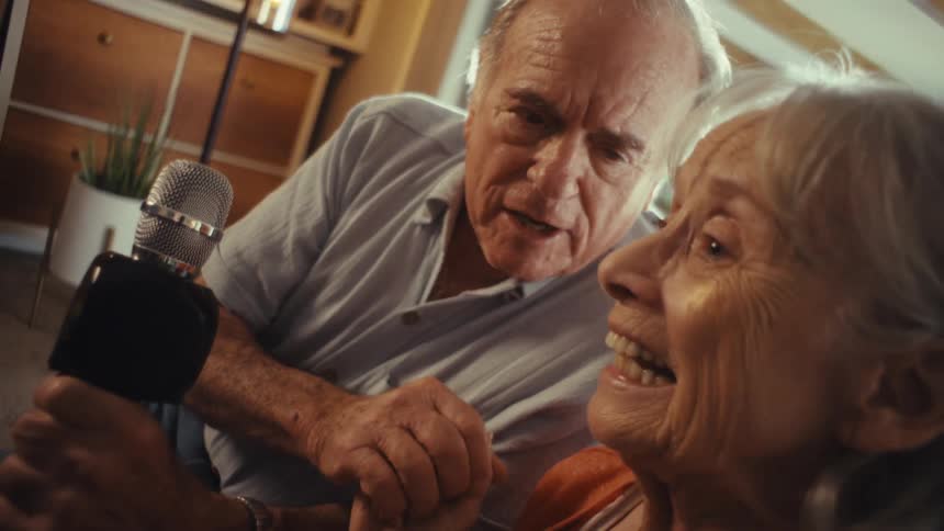 A man and woman sing into the microphone at home