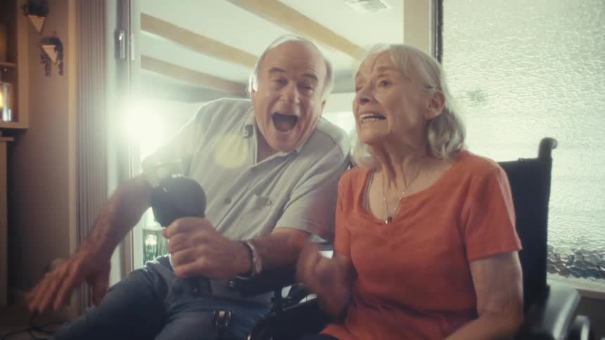 Elderly couple using a microphone while sitting at home cheers