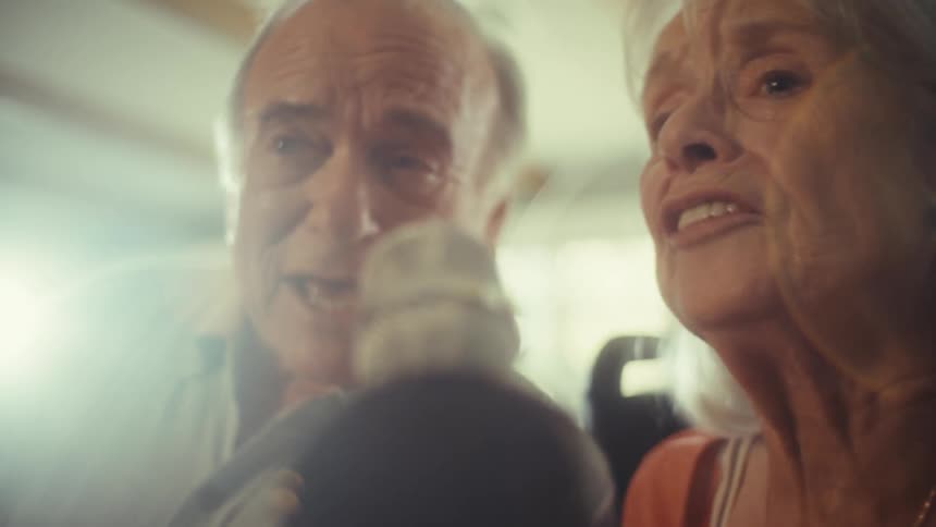Elderly couple smiles while sitting at home and talking on a microphone