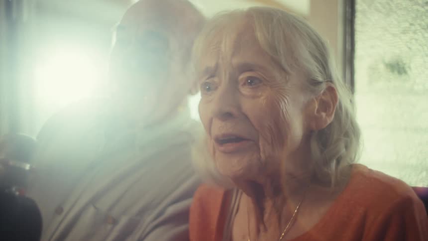 Elderly couple sitting at home during the daytime smiles while using a microphone