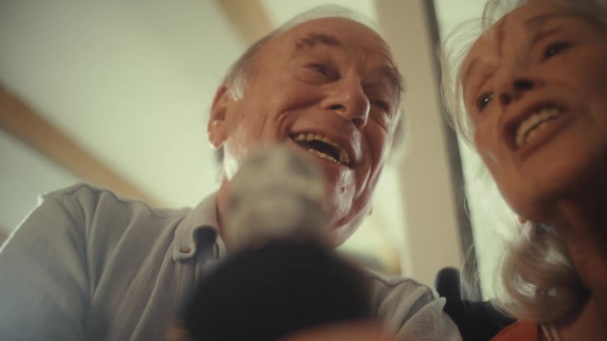 An elderly couple sings into a microphone together at home
