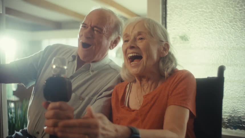 An elderly man and a woman in a wheelchair have a wonderful time singing karaoke together laughing and enjoying the moment as a bright light flashes from the microphone