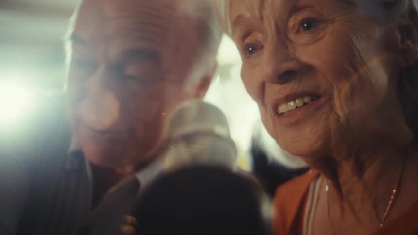 An elderly couple singing and having fun mith a microphone on an indoor setting