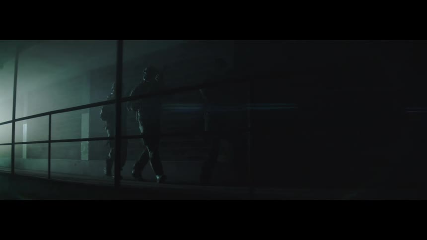 In a dark foggy room several people are visible in the background appearing as shadowy figures they are holding what look like assault rifles