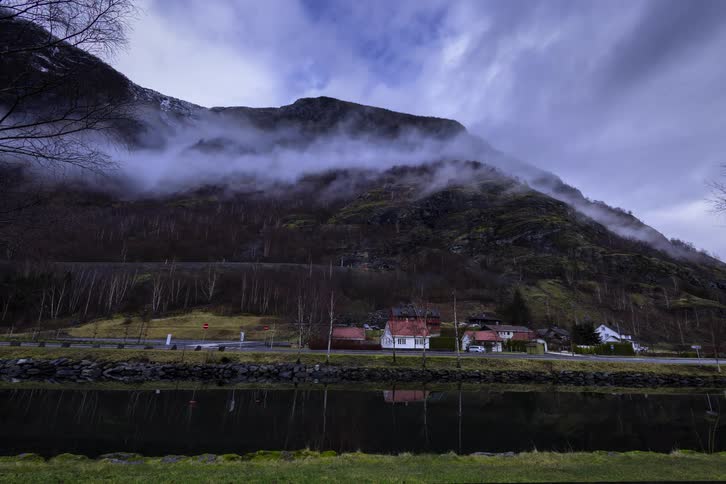 A landscape displays a mountain and a body of water with a road and a building between them