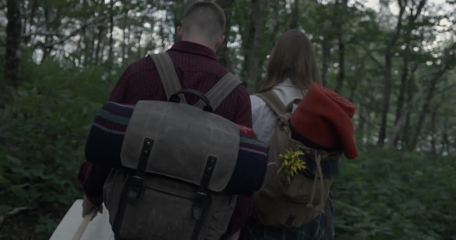 A man and woman carry items up a forest trail