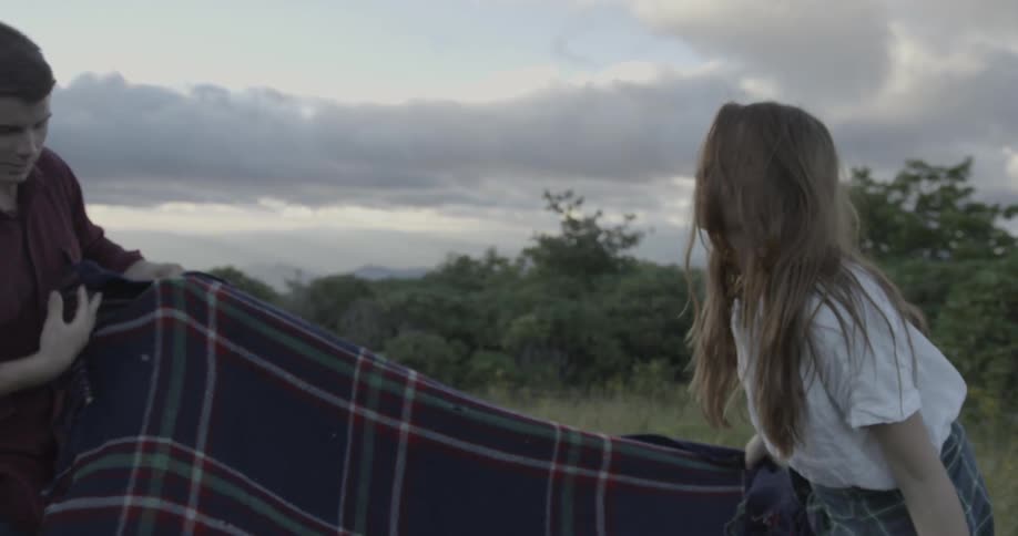 Couple helping each other spread out a blanket for a picnic