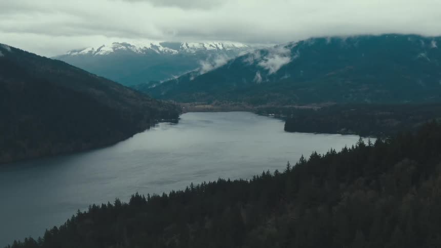 Aerial view of a lake surrounded by forests and mountains under cloudy sky
