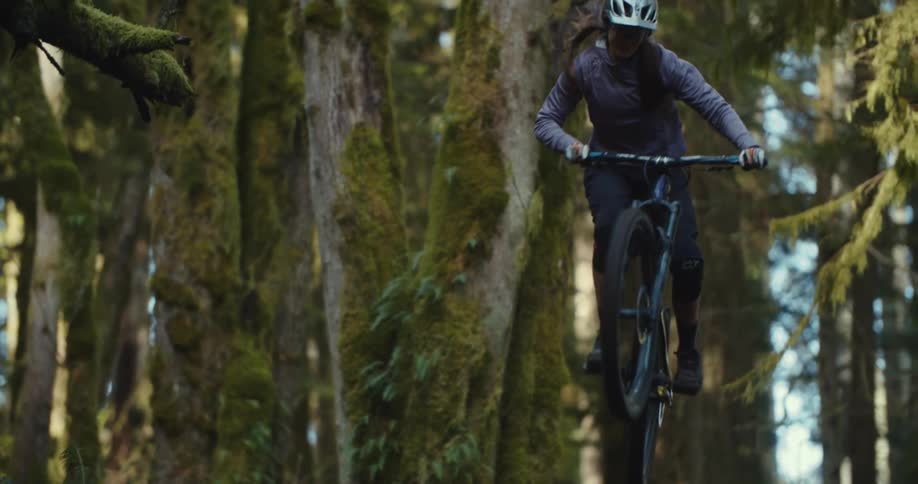 The woman jumps on a hill in the forest with her mountain bike