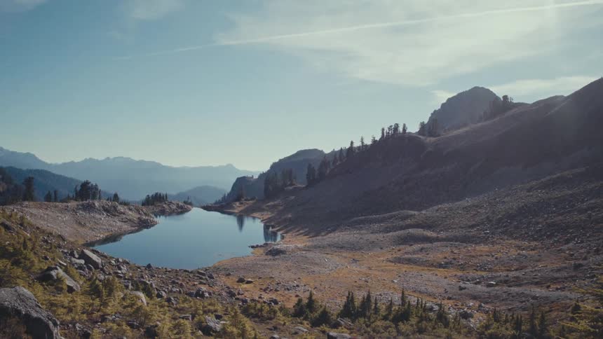 Sunlight shines onto a valley containing a small reflective lake on a foggy day