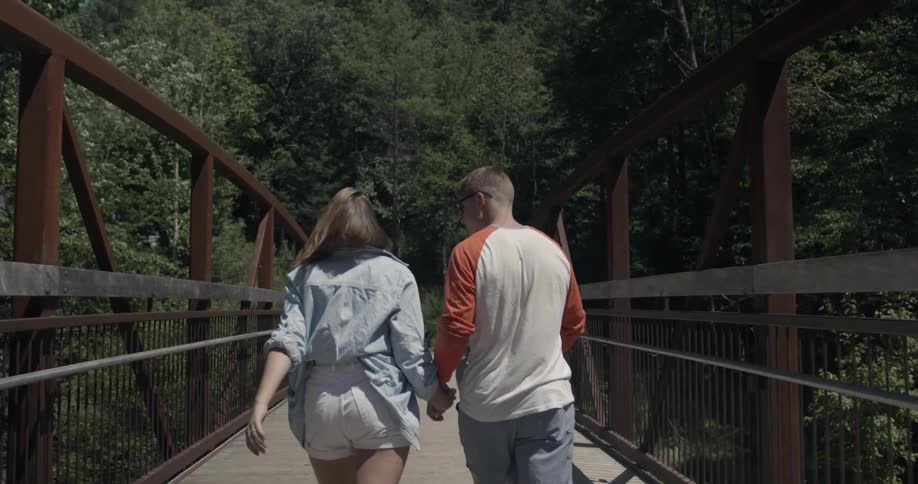 Man and woman holding hands while walking across footbridge