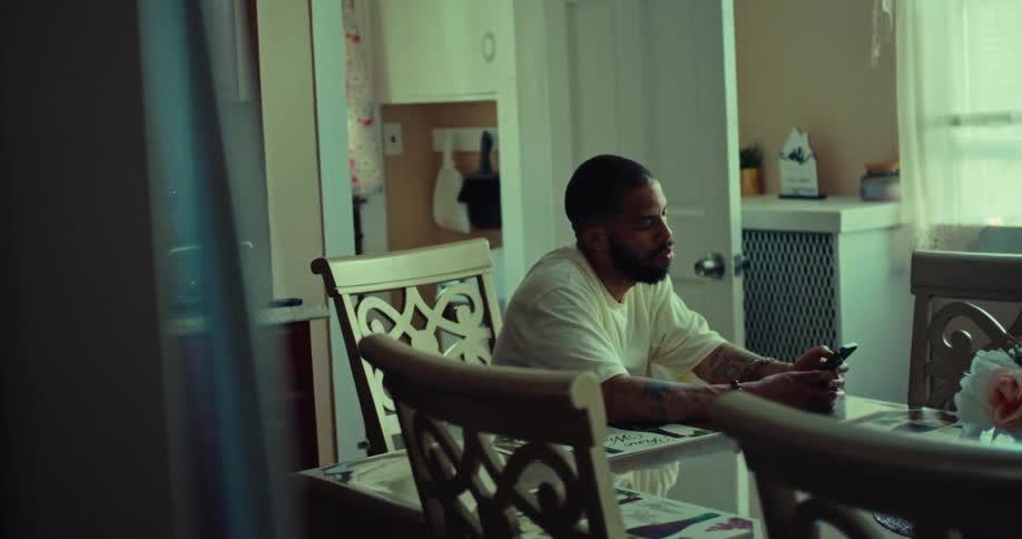 A person sits at a dining room table with a phone and rests their head on their hand
