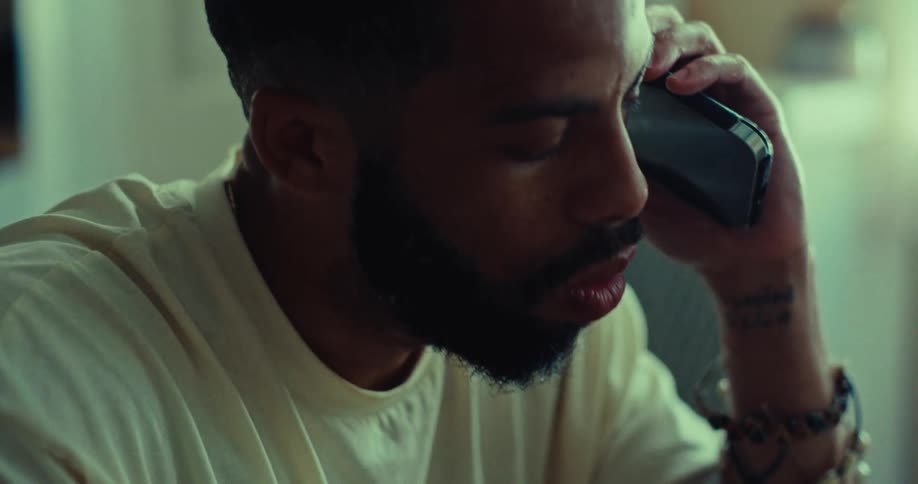 A bearded person is sitting with their head in their hand looking sad or worried they then bring a cell phone to their ear as if answering a call