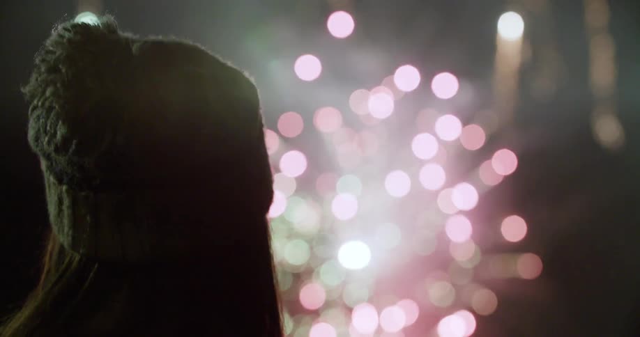 A person watches fireworks in the darkness