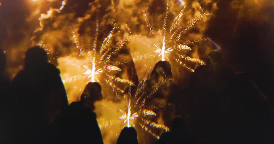 Group of people watch golden fireworks bursting in the bright sky