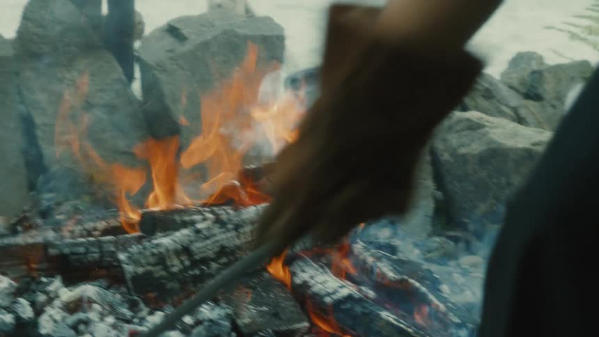 Person stirring a charcoal fire outdoors roasting meat