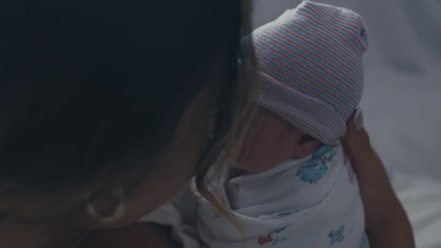 A mother cuddling her newborn baby in an indoor setting