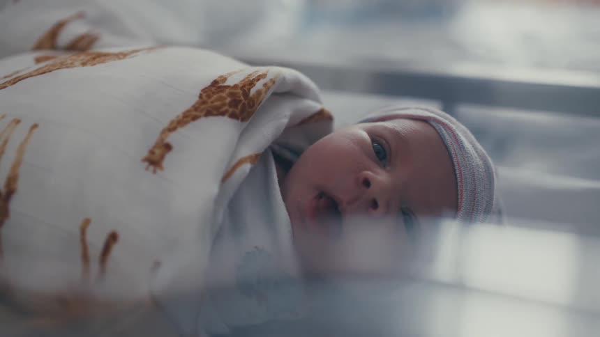 Newborn baby wrapped in a blanket yawning on a baby bed indoors during day time