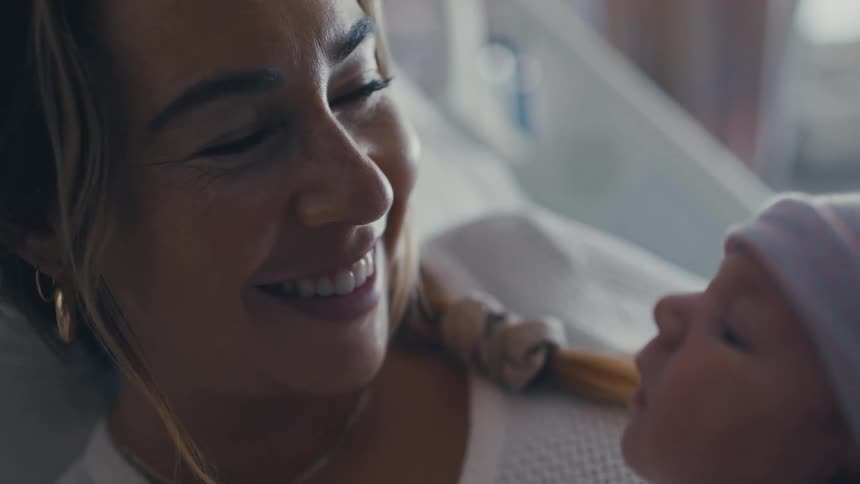 A woman lies on a bed and smiles at an infant in her arms