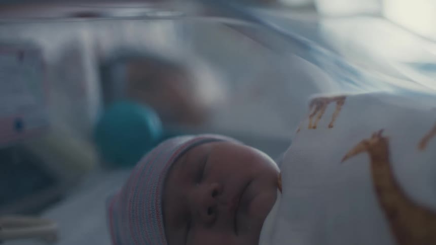 Newborn sleeps in a bassinet while their mother sleeps in her hospital bed