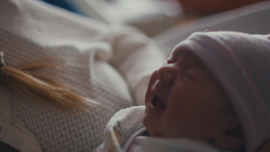 Mother lying in a hospital bed smiles while holding her newborn
