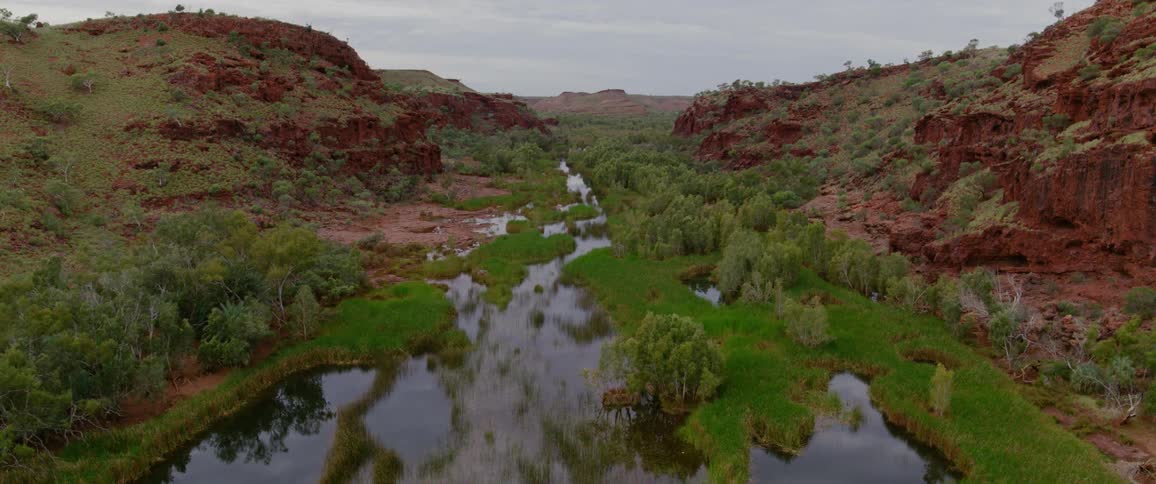 An aerial view shows a serene river winding through a lush green valley flanked on both sides by striking red rock canyons the calm water perfectly reflects the sky and surrounding foliage