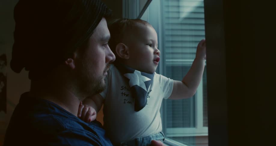 A man holds a baby looking out a window