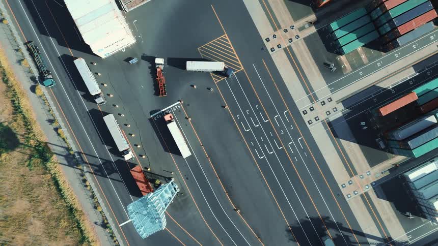 Aerial view of trucks maneuvering on marked lanes inside a port terminal