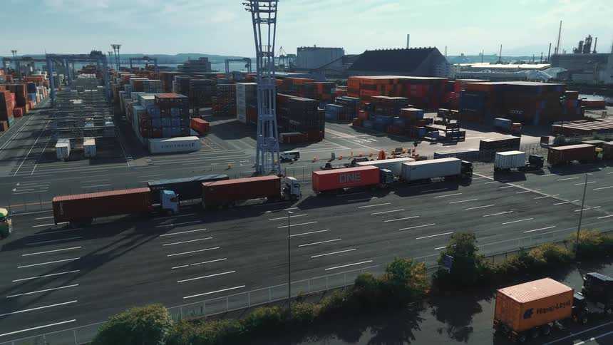 A line of trucks parked in a large cargo shipping container depot