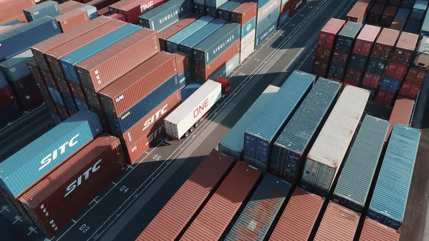 An aerial view shows a semitruck driving through a bustling container yard filled with stacks of shipping containers the containers are arranged in long neat rows ready for transport