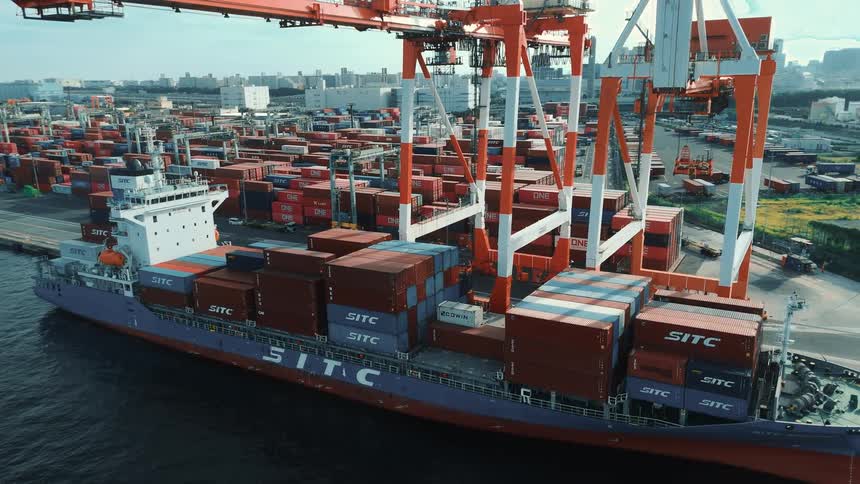 A cargo ship is docked at a port while cranes load and unload shipping containers