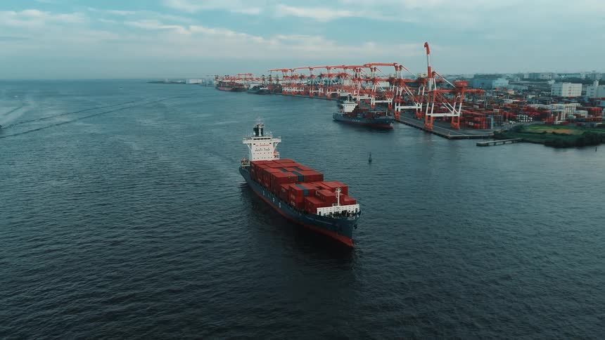 Ship with containers sailing on the ocean with the port in the background
