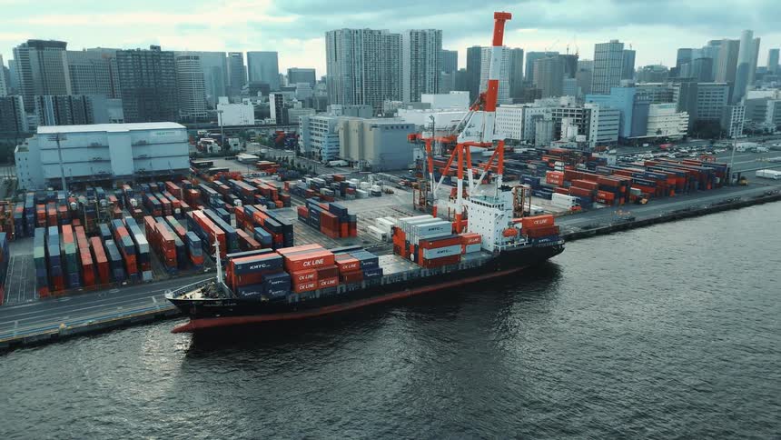 Freight ship full of containers docked on a port next to a metropolitan area outdoors during day time