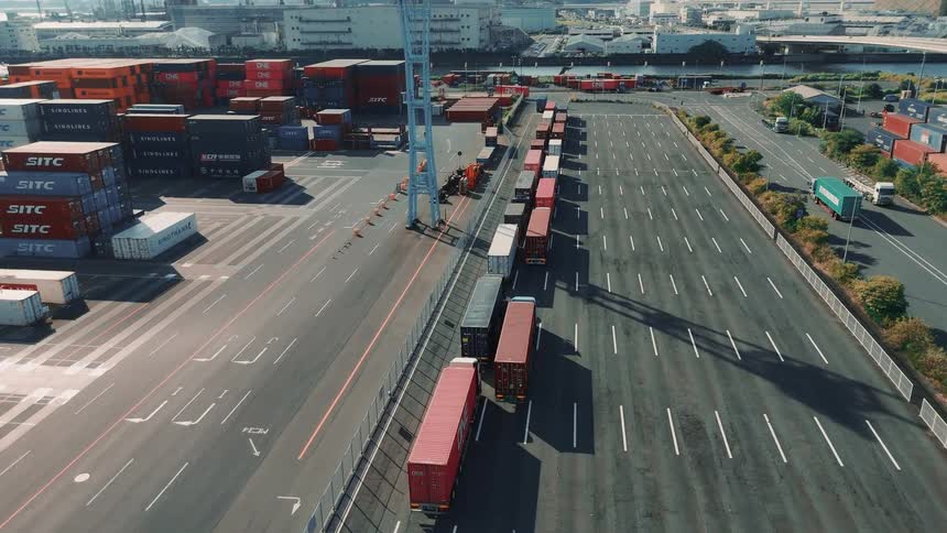 Line of trucks with containers parked beside organized stacks in the port terminal