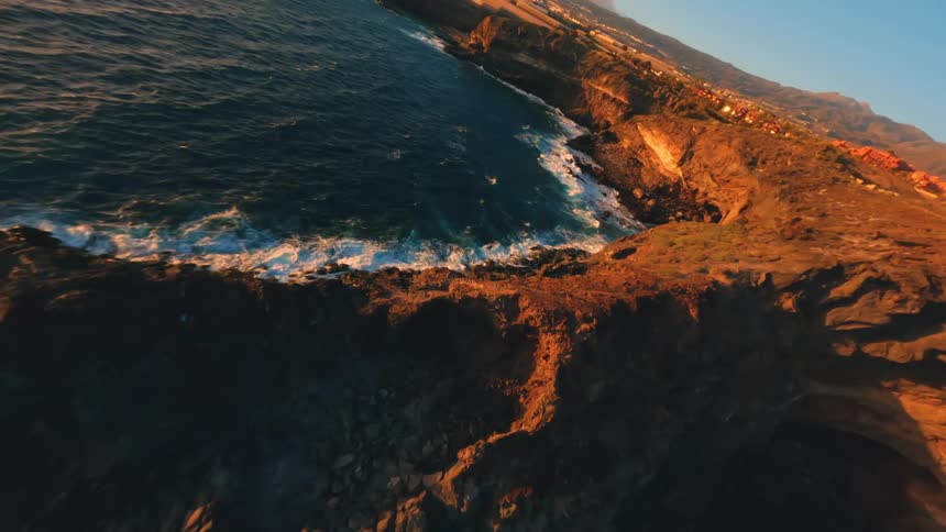 Flying fast over a rocky coast with the sea waves hitting the rocks with force